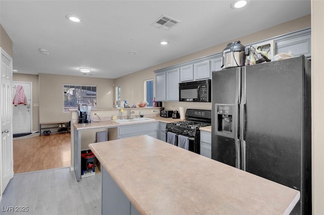 kitchen featuring gray cabinets, black appliances, kitchen peninsula, sink, and light hardwood / wood-style flooring