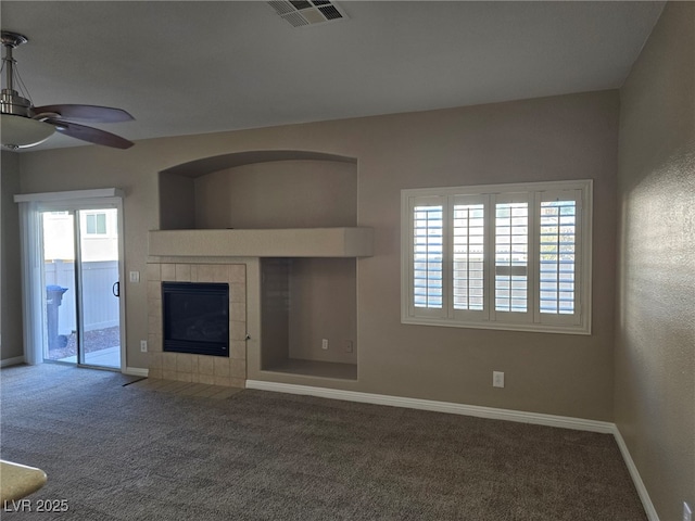 unfurnished living room with ceiling fan, carpet floors, visible vents, baseboards, and a tiled fireplace