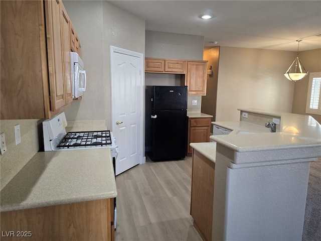 kitchen featuring white appliances, light wood finished floors, light countertops, pendant lighting, and a sink