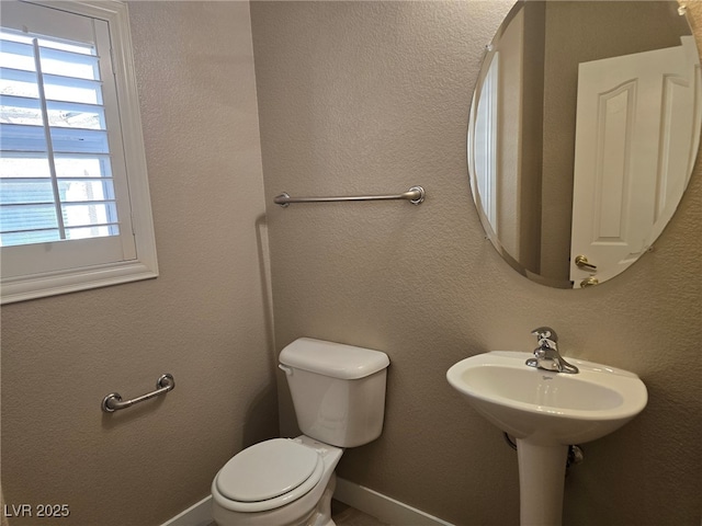 half bathroom featuring a textured wall, a sink, toilet, and baseboards