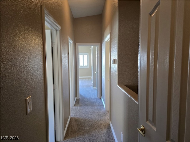 corridor featuring light carpet, a textured wall, and baseboards