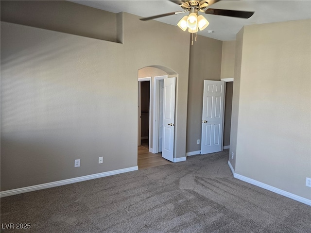 unfurnished bedroom featuring a ceiling fan, arched walkways, carpet flooring, and baseboards