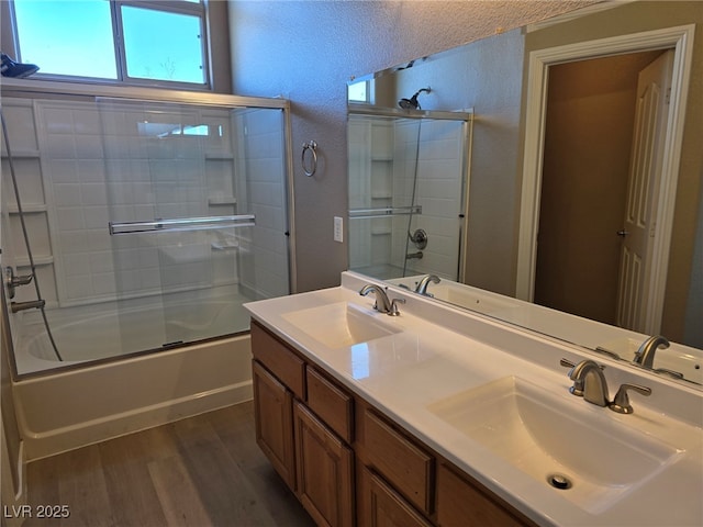 full bath featuring a textured wall, shower / bath combination with glass door, a sink, and wood finished floors