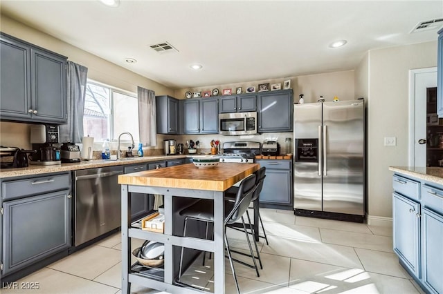 kitchen with appliances with stainless steel finishes, sink, light tile patterned floors, and wood counters