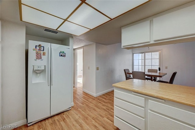 kitchen with white cabinetry, white refrigerator with ice dispenser, and light hardwood / wood-style flooring