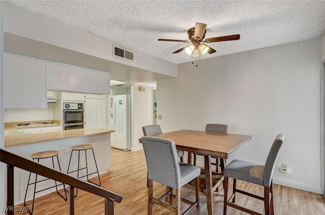 dining room with ceiling fan, a textured ceiling, and light hardwood / wood-style floors