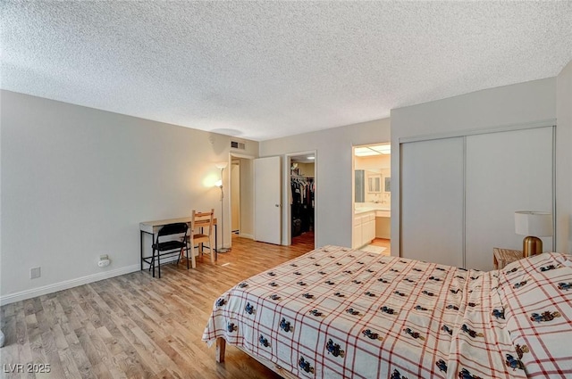 bedroom featuring connected bathroom, a textured ceiling, and light hardwood / wood-style floors