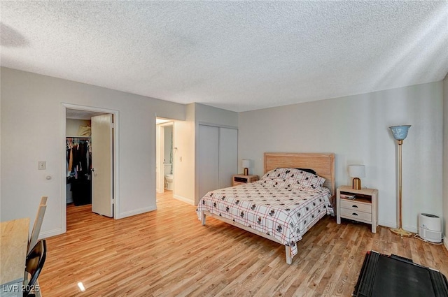 bedroom featuring a textured ceiling, ensuite bathroom, and light hardwood / wood-style flooring