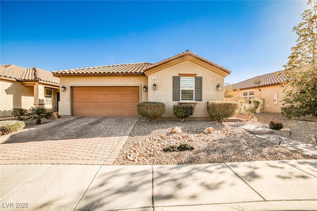 mediterranean / spanish house featuring a garage, decorative driveway, a tile roof, and stucco siding