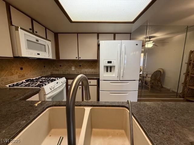 kitchen featuring sink, dark stone countertops, tasteful backsplash, and white appliances