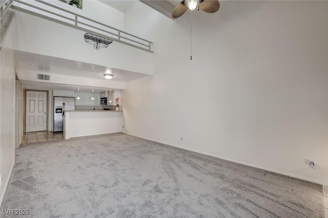 unfurnished living room with ceiling fan, light colored carpet, and a high ceiling