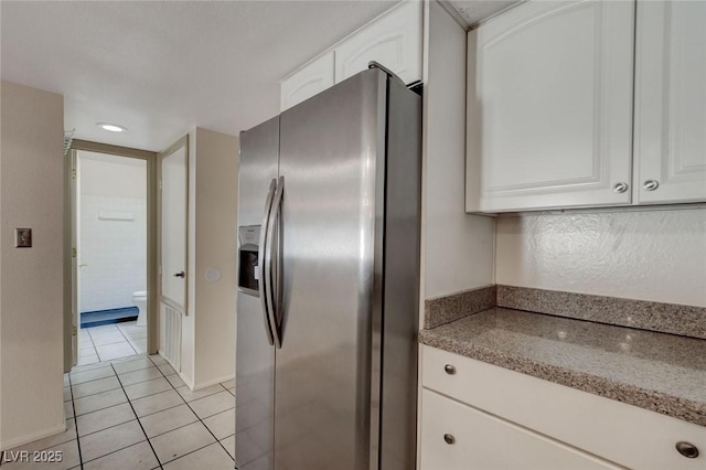 kitchen featuring light tile patterned floors, light stone countertops, white cabinets, and stainless steel fridge with ice dispenser