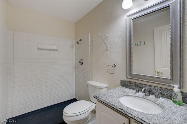 bathroom with toilet, a tile shower, and vanity