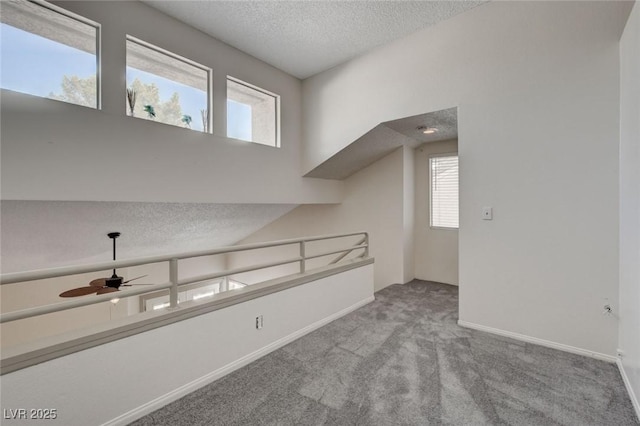 interior space with a textured ceiling, ceiling fan, and light colored carpet