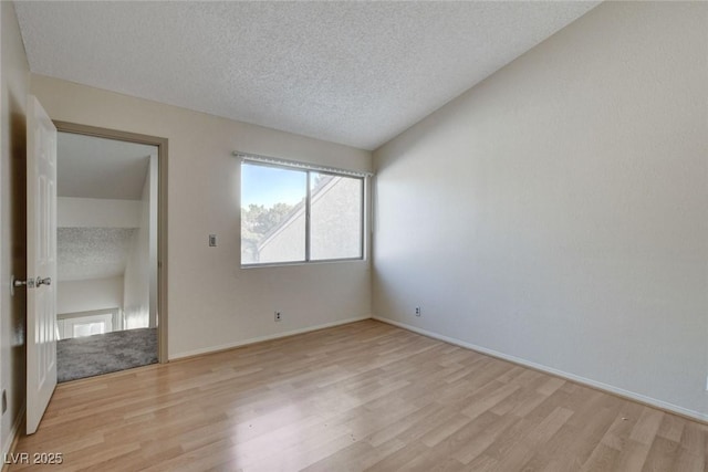 unfurnished room featuring a textured ceiling, vaulted ceiling, and light hardwood / wood-style floors