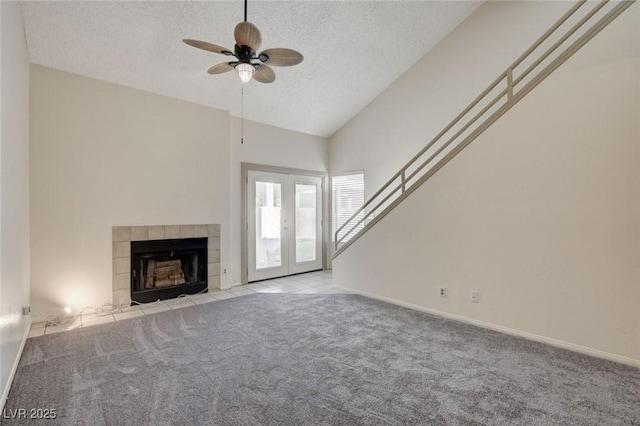 unfurnished living room with ceiling fan, a tile fireplace, a textured ceiling, light carpet, and french doors