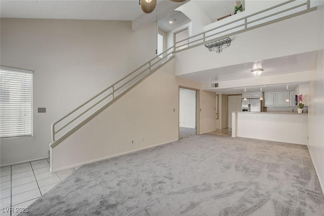 unfurnished living room with ceiling fan, light carpet, and a high ceiling