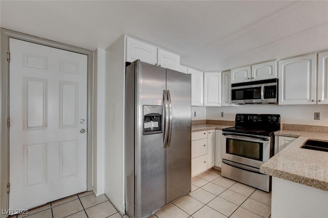 kitchen with light tile patterned floors, appliances with stainless steel finishes, a textured ceiling, white cabinets, and sink