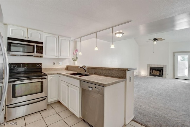 kitchen featuring white cabinetry, appliances with stainless steel finishes, a tile fireplace, and light carpet