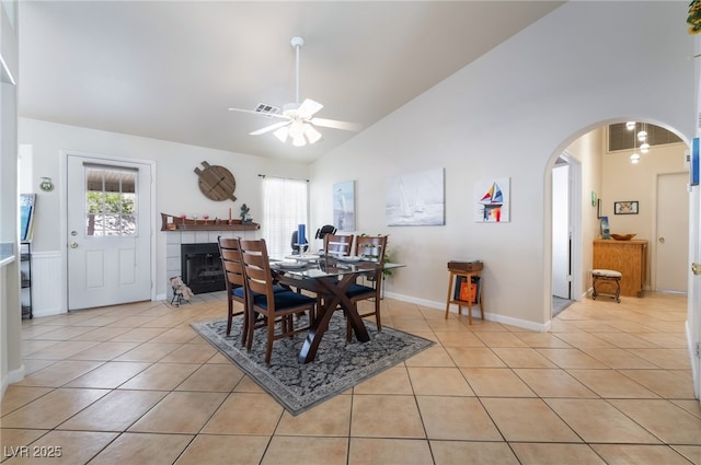 tiled dining space featuring ceiling fan, a tiled fireplace, and high vaulted ceiling