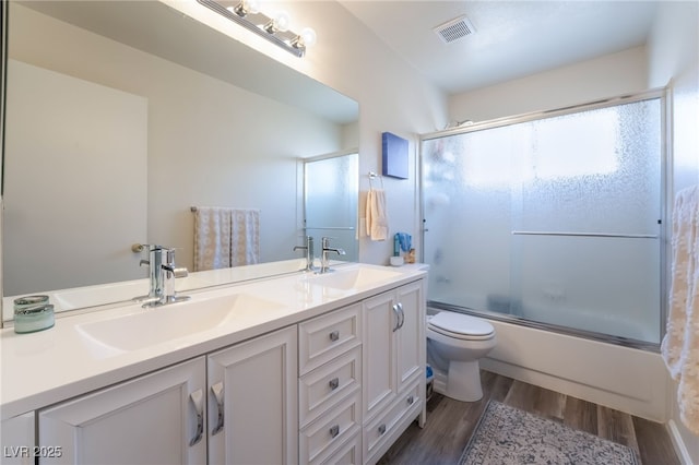 full bathroom featuring toilet, bath / shower combo with glass door, hardwood / wood-style flooring, and vanity