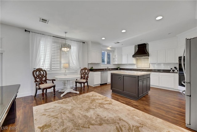 kitchen with pendant lighting, white cabinets, a center island, stainless steel appliances, and premium range hood