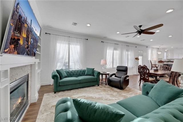 living room featuring ceiling fan, crown molding, hardwood / wood-style floors, and a stone fireplace