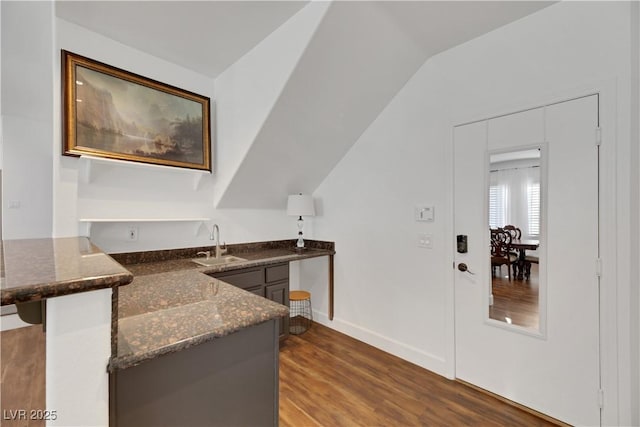 bar featuring lofted ceiling, dark stone counters, sink, dark hardwood / wood-style floors, and gray cabinetry