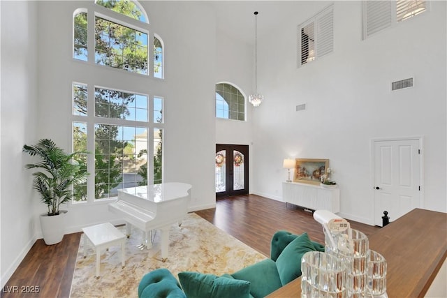 living room featuring french doors, dark hardwood / wood-style flooring, a towering ceiling, and a notable chandelier