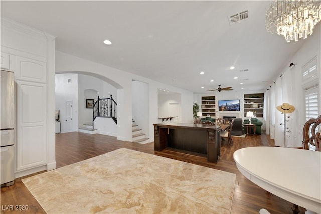 interior space featuring ceiling fan with notable chandelier, dark hardwood / wood-style floors, and built in shelves