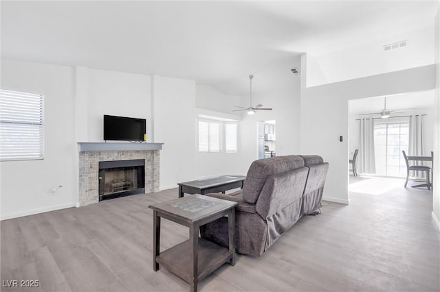 living room featuring lofted ceiling, a tile fireplace, light hardwood / wood-style floors, and ceiling fan