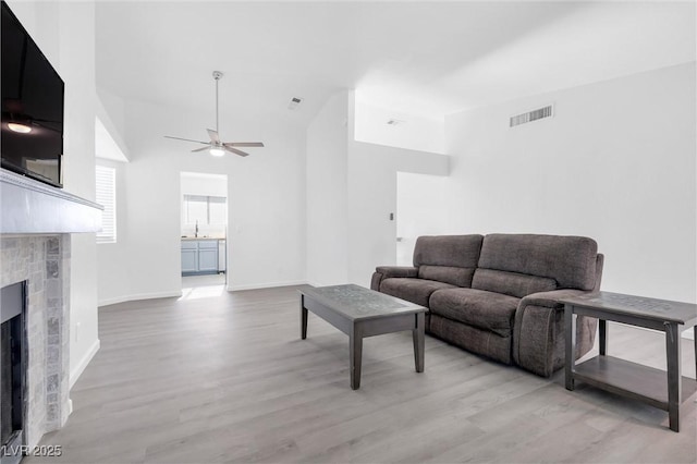 living room featuring a fireplace, sink, light hardwood / wood-style flooring, and ceiling fan