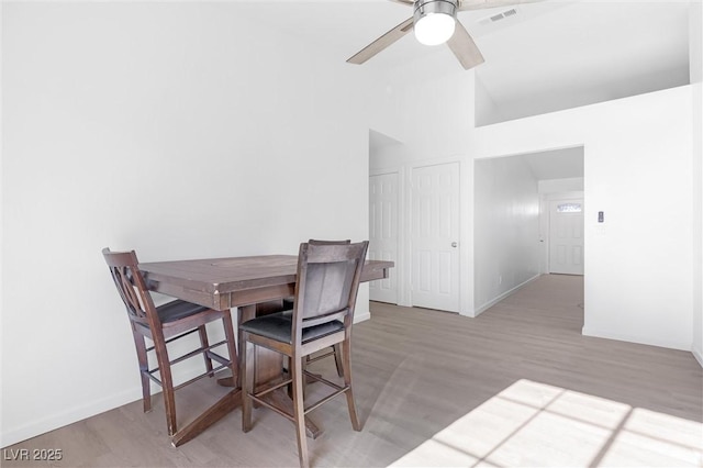 dining area featuring ceiling fan, light hardwood / wood-style flooring, and a towering ceiling