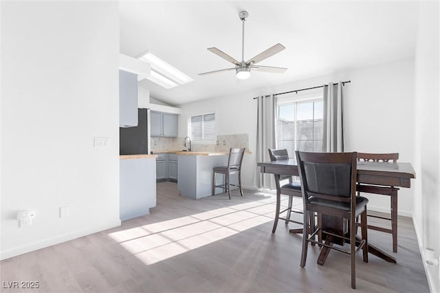 dining space featuring ceiling fan, sink, lofted ceiling, and light wood-type flooring