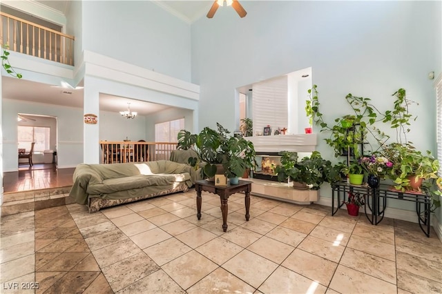 living room featuring ceiling fan with notable chandelier, ornamental molding, a fireplace, and a high ceiling