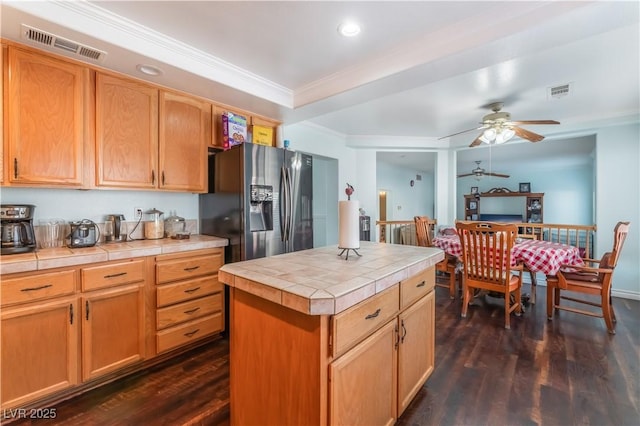 kitchen featuring dark hardwood / wood-style floors, a kitchen island, ornamental molding, tile counters, and stainless steel fridge