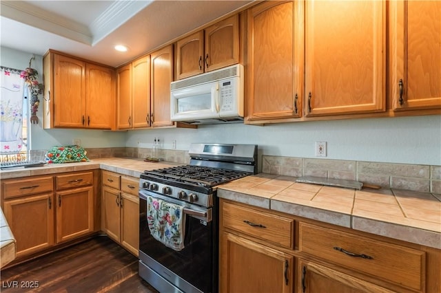 kitchen with tile countertops, a raised ceiling, dark wood-type flooring, ornamental molding, and stainless steel gas stove