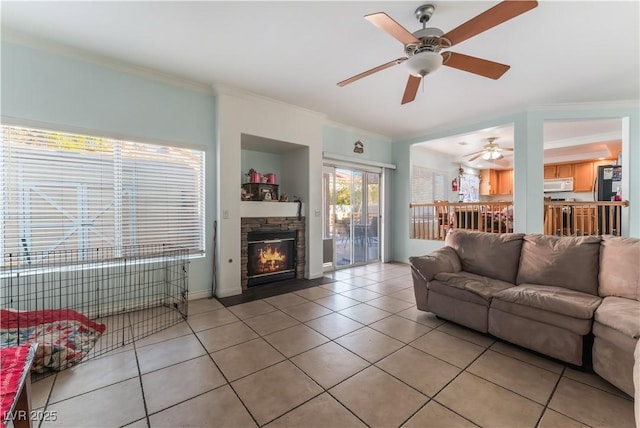 living room featuring ceiling fan, light tile patterned floors, crown molding, and a stone fireplace