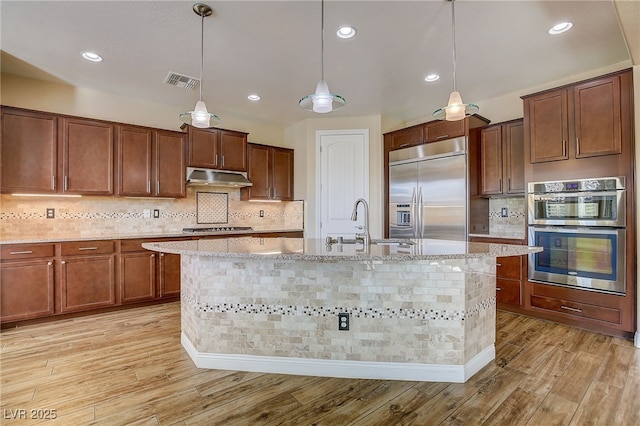 kitchen featuring decorative light fixtures, light hardwood / wood-style floors, appliances with stainless steel finishes, and a center island with sink