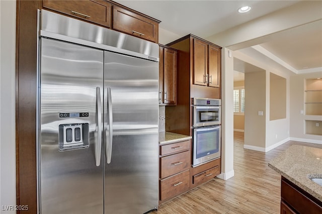 kitchen featuring light wood-type flooring, built in shelves, appliances with stainless steel finishes, and light stone countertops