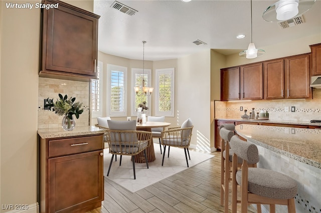 kitchen featuring light stone counters, backsplash, and hanging light fixtures