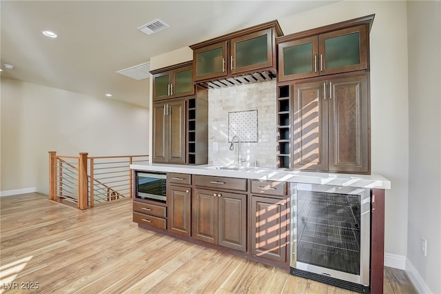 bar featuring light hardwood / wood-style floors, sink, beverage cooler, and stainless steel microwave