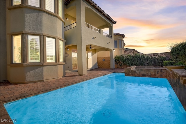 pool at dusk featuring ceiling fan and an in ground hot tub