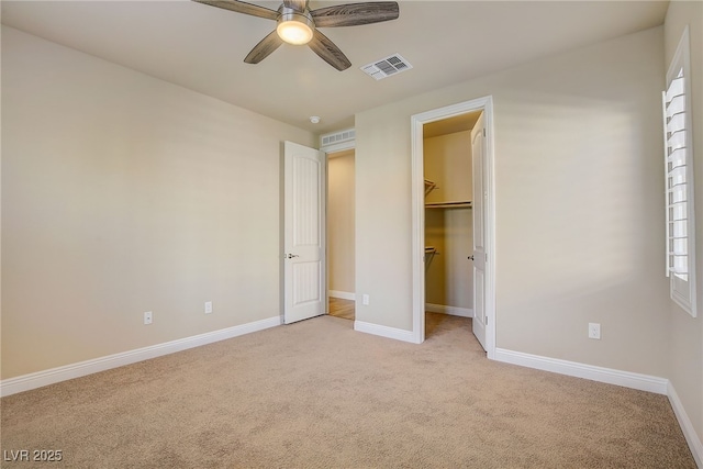 unfurnished bedroom featuring ceiling fan, light carpet, a spacious closet, and a closet