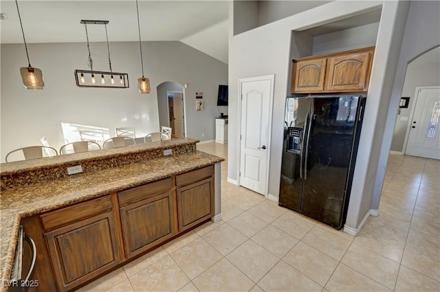 kitchen featuring black refrigerator with ice dispenser, stone counters, light tile patterned flooring, and decorative light fixtures