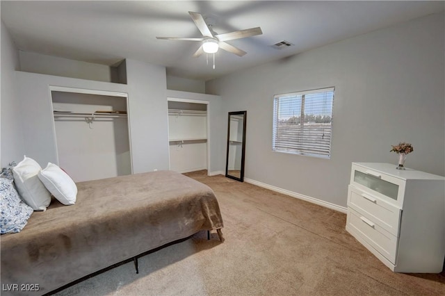 bedroom with ceiling fan, light colored carpet, and multiple closets