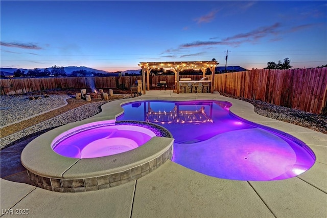 pool at dusk with an in ground hot tub, a patio area, exterior bar, a mountain view, and a pergola