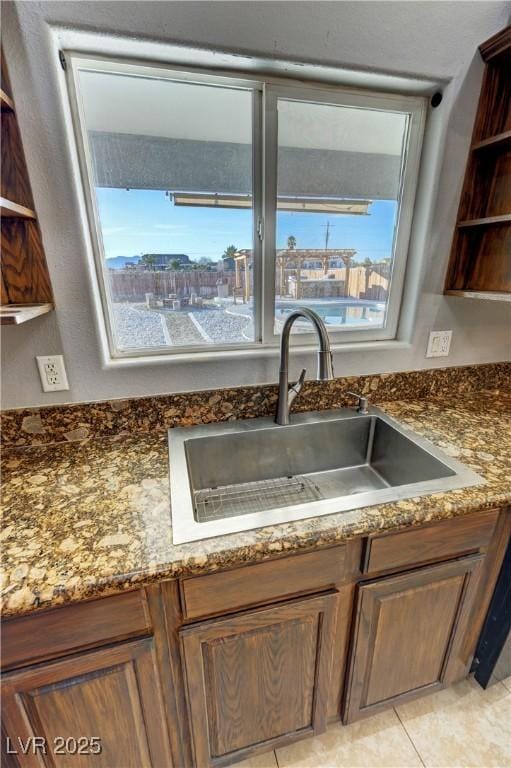 kitchen with dark stone countertops, sink, light tile patterned floors, and a healthy amount of sunlight