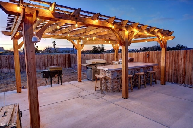 patio terrace at dusk with a bar, an outdoor kitchen, grilling area, and a pergola