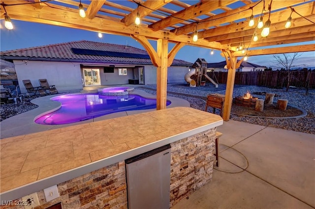 pool at dusk with a pergola, a patio area, a playground, exterior bar, and area for grilling